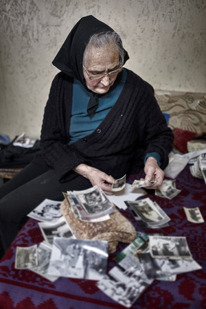 Nostalgic old woman looking at vintage photosの写真素材