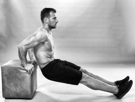 Fitness trainer doing pushups on gray background in studio