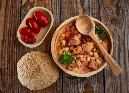Wooden bowl and spoon with smoked pork leg and beans stew on a rustic tableの写真素材