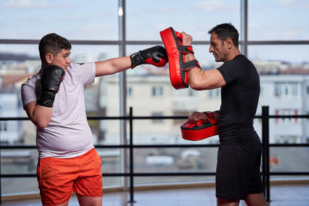 Overweight young kickboxer hitting mitts with his coach