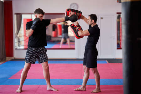 Young kickboxing fighter hitting mitts with his coach in the gymの写真素材