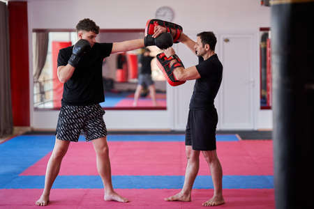 Foto de Young kickboxing fighter hitting mitts with his coach in the gym - Imagen libre de derechos