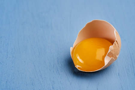 Raw egg and broken shell on blue backgroundの写真素材