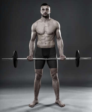 Young athletic man training with a barbell isolated on gray backgroundの写真素材