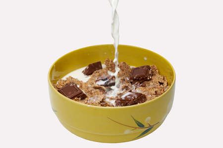 Pouring milk over oat cornflakes with chocolate on a bowl, perfectly isolated on white backgroundの写真素材