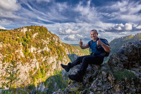 Hiker with backpack on the edge of a cliff in the mountainsの写真素材