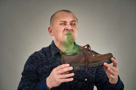 Caucasian man holding a stinking shoe with an expression of disgustの写真素材
