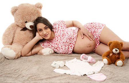 Pregnant woman with toys and baby clothing on a blanket