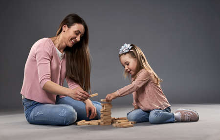 Mother and little daughter playing with cubes, studio shot on gray backgroundの写真素材
