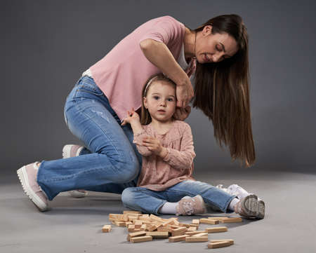 Mother and little daughter playing with cubes, studio shot on gray backgroundの写真素材