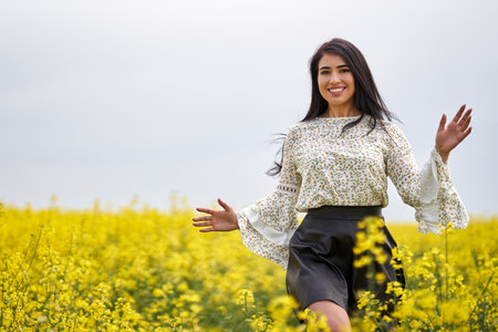 Beautiful brunette hispanic young woman in a blooming canola fieldの写真素材