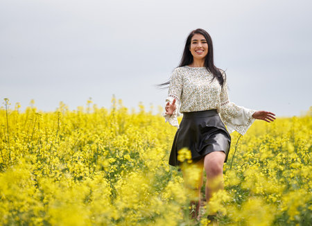 Beautiful brunette hispanic young woman in a blooming canola fieldの写真素材