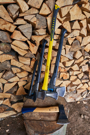 Many light and heavy axes on a stump by a stack of firewood