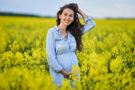 Happy young pregnant woman in a canola fieldの写真素材