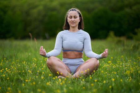 Confident beautiful plus size woman doing yoga in a field by the forest