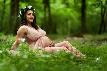 Portrait of a beautiful young hispanic pregnant woman in a deciduous forest in the summerの写真素材