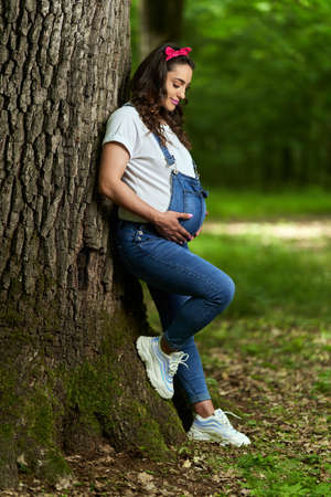 Portrait of a beautiful young hispanic pregnant woman in a deciduous forest in the summerの写真素材
