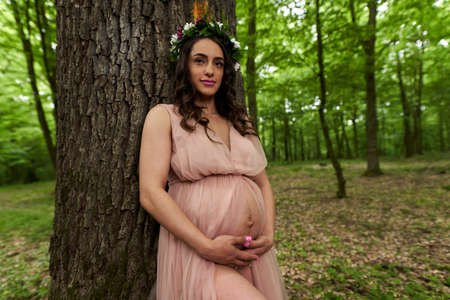Portrait of a beautiful young hispanic pregnant woman in a deciduous forest in the summerの写真素材