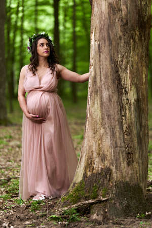 Portrait of a beautiful young hispanic pregnant woman in a deciduous forest in the summerの写真素材