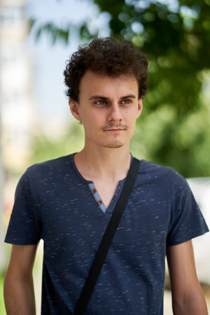 Closeup of a handsome young trendy man with curly hair outdoor in the city park