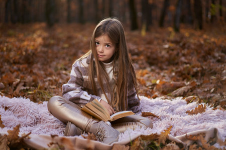 Candid portrait of a young girl in late November in the colorful oak forest, reading a bookの写真素材