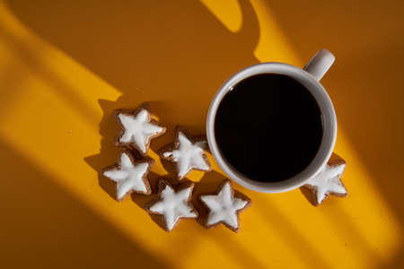A coffee cup with Christmas biscuits in the morning, on yellow background