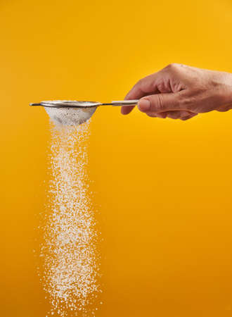 Woman's hand sprinkling powdered sugar with a sifter, isolated on yellow backgroundの写真素材