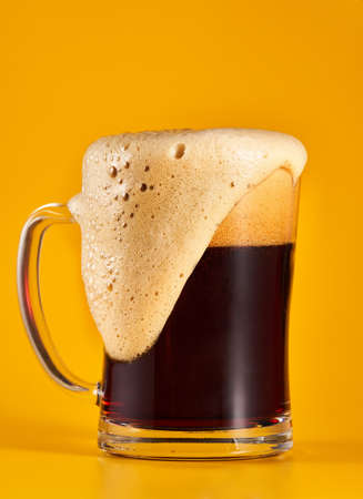 Dark brown beer in a half liter glass mug isolated on yellow background