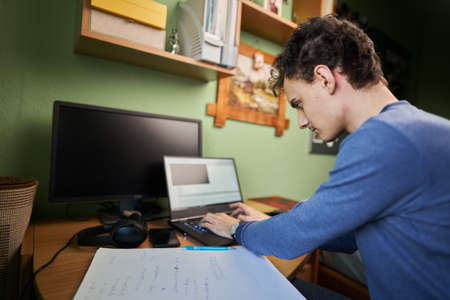 Software developer student working from home with laptop, computer, cellphone and notebook for his...