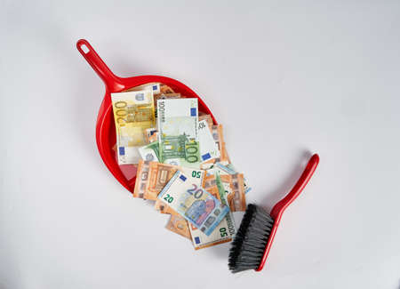 Clearing out dirty money with the brush in a dustpan, isolated on whiteの写真素材