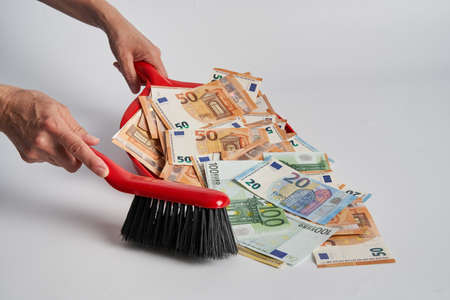Clearing out dirty money with the brush in a dustpan, isolated on whiteの写真素材