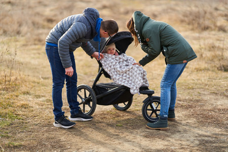 Young family with their little baby girl walking through park with baby carriage in a residential areaの写真素材