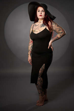 Size plus beautiful woman with tattoos, black dress and hat, glamour shotの写真素材