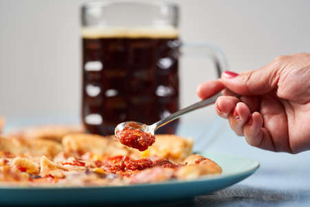 Woman spreading sauce on pizza with a dark beer in backgroundの写真素材