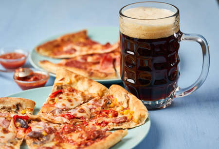 Dark beer in a mug and pizza slices on blue backgroundの写真素材