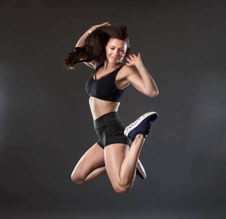 Athletic woman jumping high, freeze motion on gray backgroundの写真素材