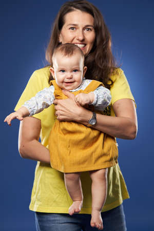 Young mother having a great time with her baby daughter, studio shot over blue backgroundの写真素材