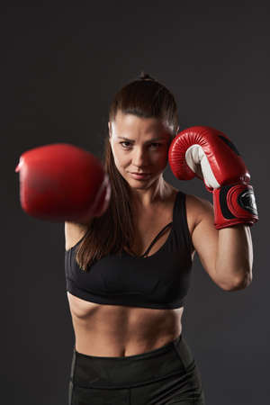 Woman boxer in red gloves delivering a right cross, isolated on gray backgroundの写真素材