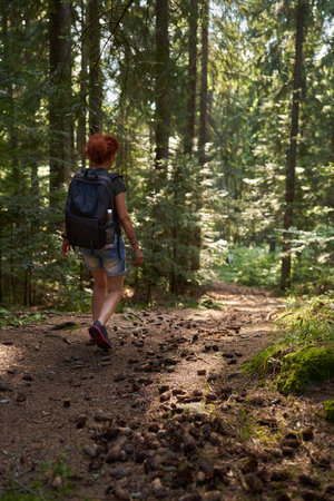Woman hiker with backpack hiking into the mountain forest