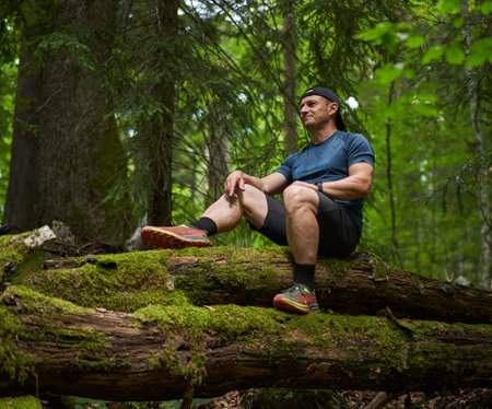 Man sitting on a tree log covered in moss after a hikeの写真素材
