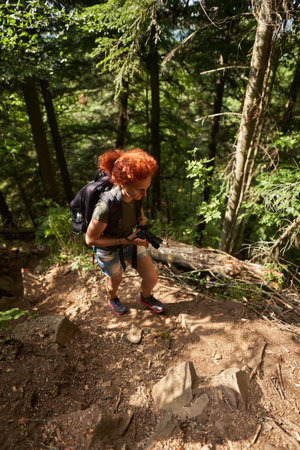 Woman hiker with backpack and camera hiking into the mountain forest