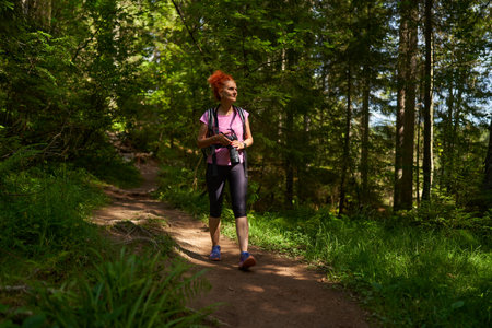 Woman hiker with backpack hiking into the mountain forest