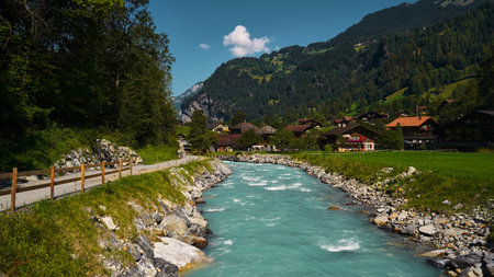 Landscape with an emerald mountain river in the Swiss Alps flanked by a road and a villageの写真素材