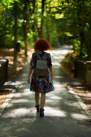 Portrait of a beautiful curly redhead woman in floral dress in the park