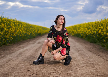Beautiful Hispanic woman in floral dress on a road between canola fields