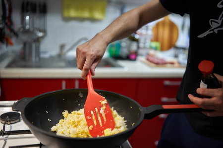 Hands of a young man making fried rice with eggs in a work, asian recipe, on a gas stoveの写真素材