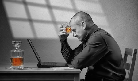 Drinking at work - business man with a glass of whisky in front of his laptop, concept of depression with everything but the alcohol being black and whiteの写真素材
