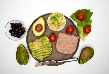 Breakfast with foie gras pate and avocado on toast with black olives aside, isolated on white backgroundの写真素材