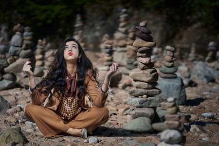 Businesswoman trying to chill after work stress, sitting among stacked zen stone pyramids on a beachの写真素材