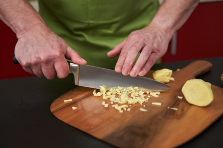 Man chef chopping ginger finely on a wooden board with a very sharp knife